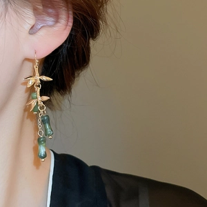 Close-up of Chinese style long earrings with green bamboo beads and golden leaf details