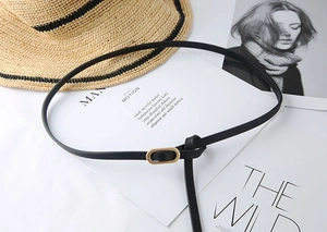 Detail of slim black leather belt with a golden oval buckle on white fashion background
