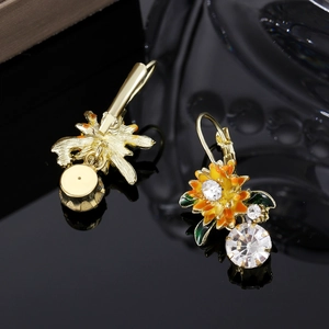 Détail de boucles d'oreilles tournesol dorées avec feuilles en émail et cristaux scintillants