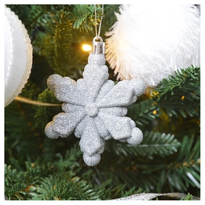 Close-up of glittery silver snowflake ornament hanging on a Christmas tree with warm lights