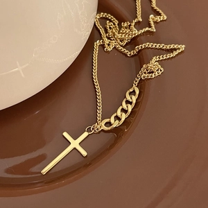 Macro detail of a gold chain necklace with cross pendant on a ceramic plate