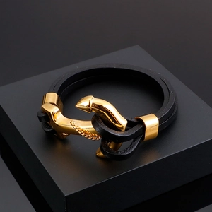 Close-up of black braided leather bracelet with a polished gold anchor-shaped metal clasp