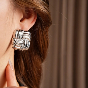 Close-up of silver square stud earrings with woven texture worn by a model