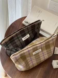 Detailed close-up of textured tweed plaid makeup bags with metal zipper on a wooden table