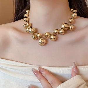 Polished gold metal bead necklace detail showing reflective round spheres on collarbone