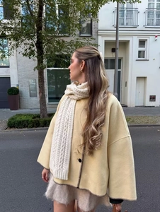 Close-up of yellow wool coat featuring black contrast stitching and knit scarf texture