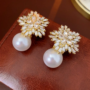 Macro detail of gold flower earrings with sparkling zircons and a large white pearl