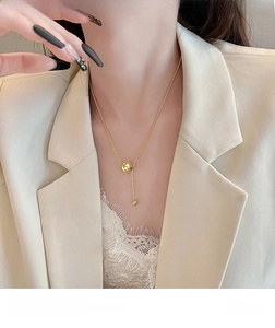 Detail of a gold titanium steel necklace featuring a minimalist ball and vertical bar pendant