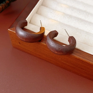 Close-up of C-shaped dark brown wooden earrings on a beige velvet jewelry tray