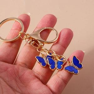 Close-up of golden butterfly keychain with blue enamel drips and sparkly rhinestones