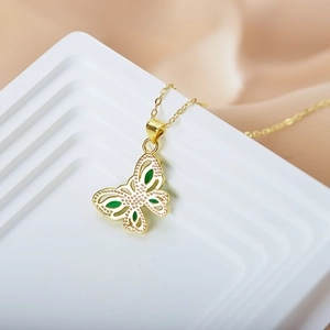 Detail view of a gold butterfly pendant with green enamel on a soft textured background