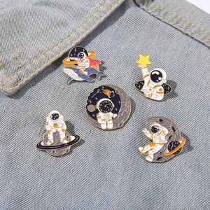 Close-up of five space-themed enamel pins featuring astronauts on blue denim fabric