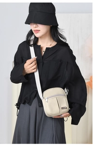 Detail of a beige nylon crossbody bag with printed wide shoulder strap on a model