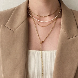Detail of layered gold link chain and white pearl necklace on woman in beige suit