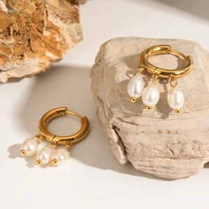 Detail of gold hoop earrings with three white teardrop pearls on a textured stone