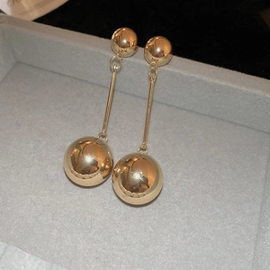Detailed view of long gold metallic drop earrings with double spheres on grey velvet