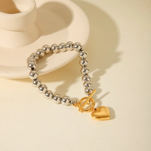 Detail of silver and gold beaded bracelet featuring a heart pendant and toggle clasp