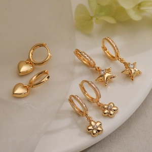 Gold earrings set with heart, star, and flower pendants on white ceramic plate