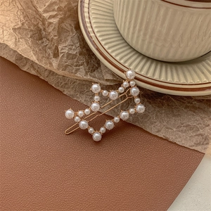 Close-up of star-shaped gold metal hair clip with white pearls on a vintage background