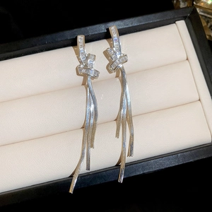 Close-up of zircon knot earrings with silver tassels on a beige display box
