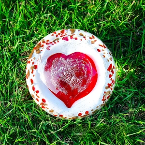 Close-up of heart-shaped glass paperweight with red center and artistic bubbles on grass
