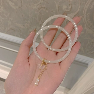 Detailed macro view of cream faux jade bangles featuring golden butterfly and pearl charms