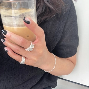Lifestyle view of irregular silver rings and chain bracelet set worn by a model holding a cup