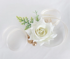 Detail of white silk rose boutonniere with gold ribbons and green leaves for wedding