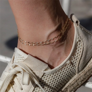 Close-up of a double-layered gold plated lace chain anklet on an ankle with sneakers