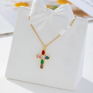 Close-up of gold-plated cross necklace with colorful zircon stones on a white stand