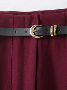 Close-up of wine red trousers featuring a black leather belt with a gold metallic buckle