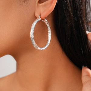 Close-up of a silver twisted rope textured geometric hoop earring worn by a model