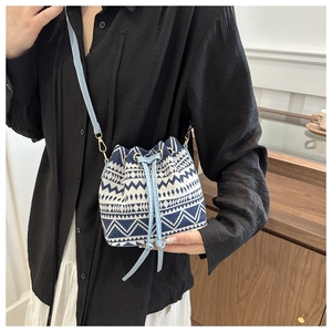 Detail of blue and white geometric drawstring bucket bag with light blue strap held by model