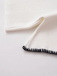 Detalle de tejido de punto blanco con costuras negras en contraste y abertura lateral
