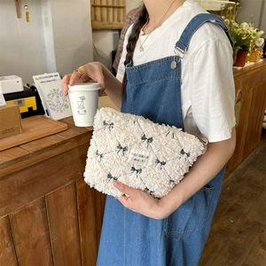 Close-up of white plush makeup bag with black bows and colorful brand woven label