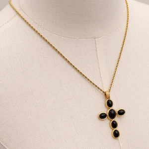 Macro detail of retro gold cross pendant with black natural stone on a rope chain