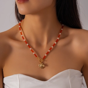 Detail of red and white beaded necklace with golden maple leaf pendant and toggle clasp