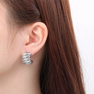 Macro side view of silver C-shaped striped earrings worn on ear showing detailed texture
