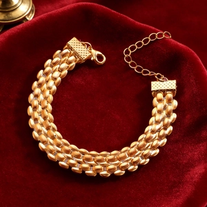 Detailed view of triple-row gold beaded bracelet with lobster clasp on red velvet