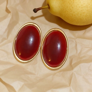 Vintage oval red resin stud earrings with gold metal frame on aesthetic paper