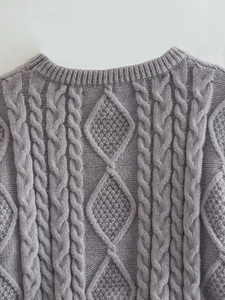 Dettaglio del maglione in maglia viola con motivi classici a trecce e a rombi