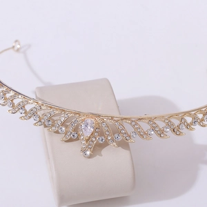 Close-up of a sparkling gold crown with clear rhinestones on a beige jewelry stand