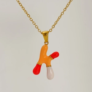 Detail view of a gold-plated letter K pendant with vibrant orange and red enamel dripping