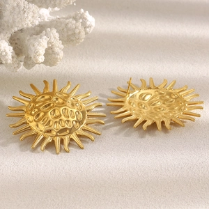 Detail of 18K gold-plated sun-shaped earrings with hammered texture on beige background