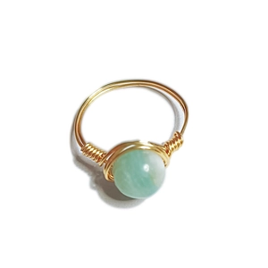 Detail of handmade gold wire-wrapped ring featuring a natural pale green stone bead