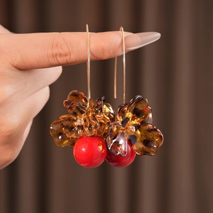 Detailed view of amber flower petal earrings with a red bead on elegant gold hooks