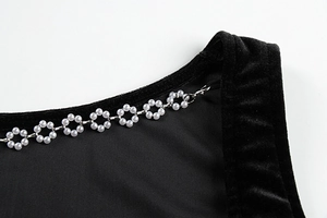 Détail macro de la chaîne de fleurs en perles blanches sur robe moulante en velours noir