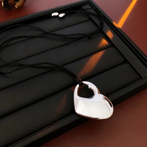 Close-up of a silver hollow double heart pendant on a black cord with light reflection
