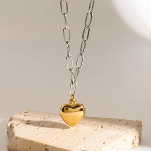 Minimalist gold heart pendant necklace on beige stone with thick silver chain link