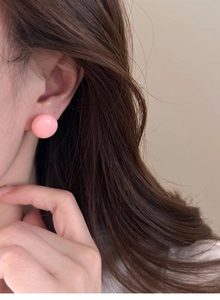 Gros plan d'une boucle d'oreille ronde rose portée à l'oreille au design minimaliste lisse